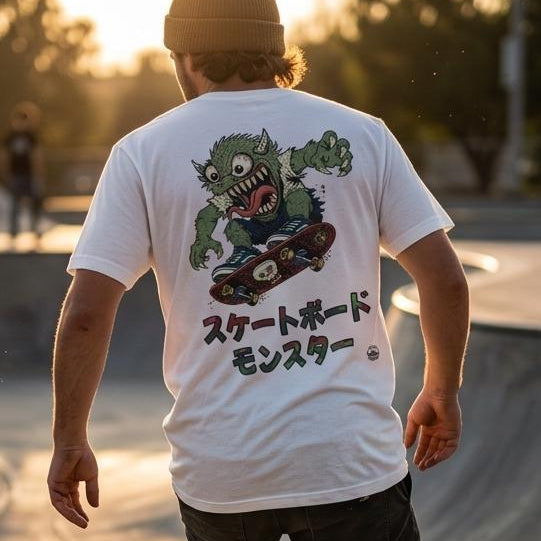 A person skateboarding in a concrete bowl at sunset, viewed from behind. The main visible product is a white graphic T-shirt with a large green monster illustration and Japanese text on the back.